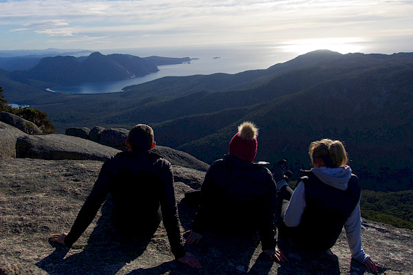 Three people sitting on a mountain looking at the scenery
