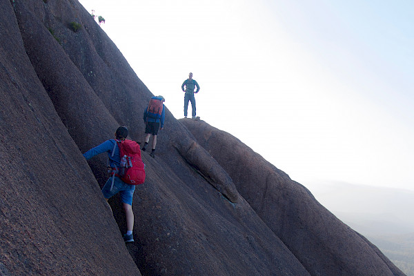 Three people walking along a steep rock face