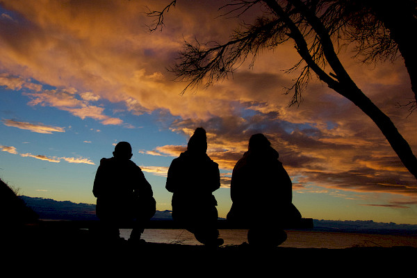 Three people sitting in silhouette, in the sunset