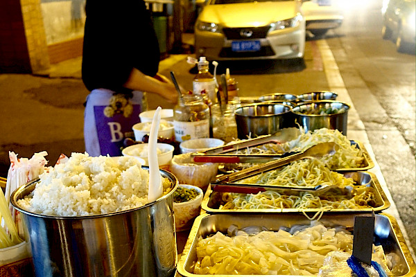 A food street vendor with a number of dishes of hot food
