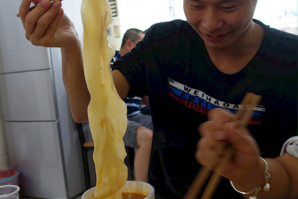 Person eating very long noodles with chopsticks