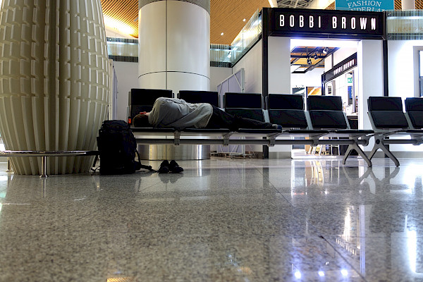 Person lying asleep over several airport lounge seats